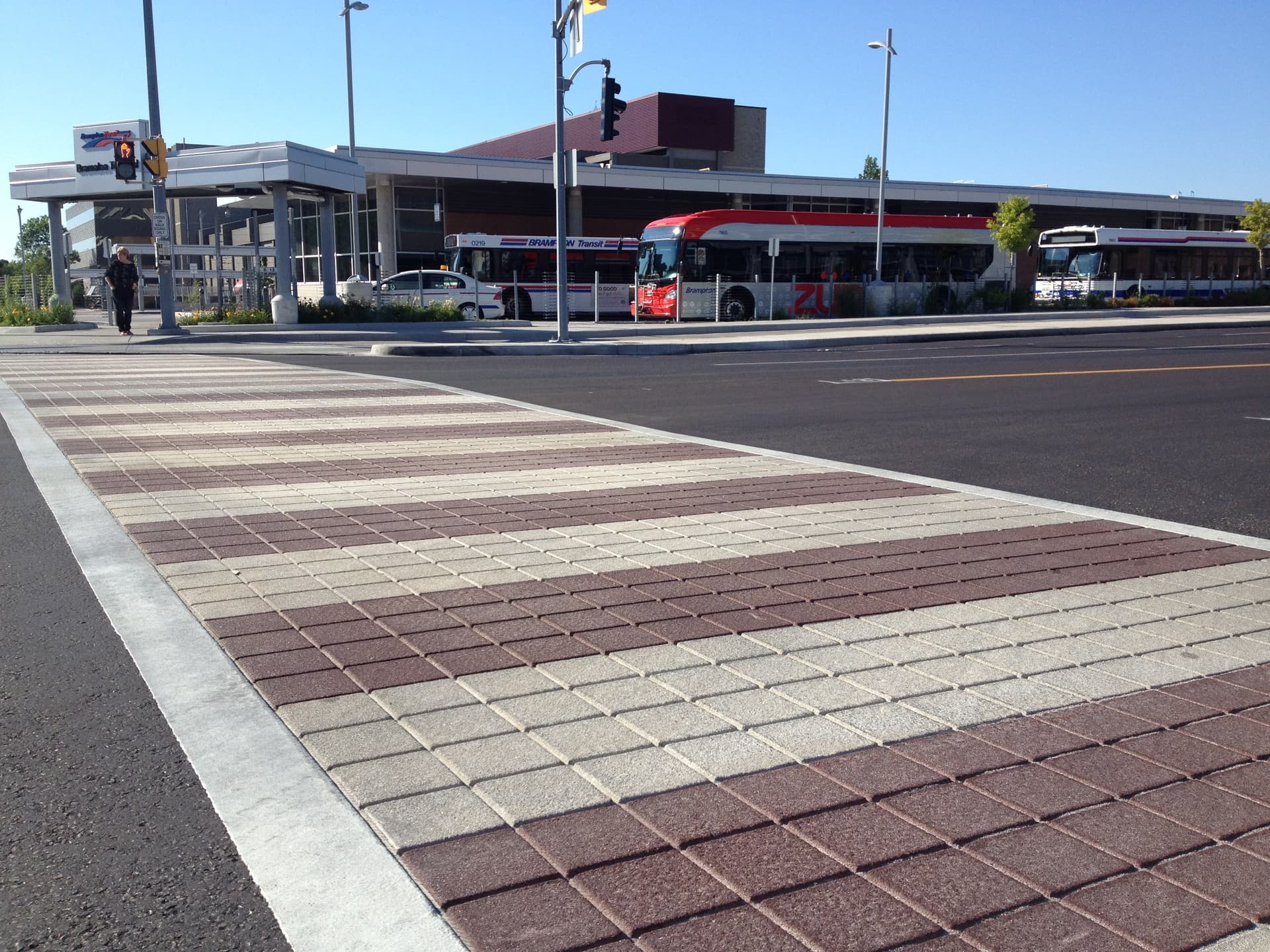 Decorative preformed thermoplastic crosswalk with white ladder bars at a transit intersection, bus passing behind — pedestrian safety surface by HUB Surface Systems